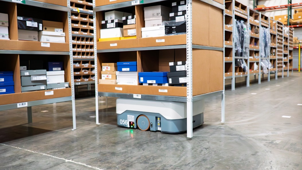 Autonomous mobile robot carrying a pallet down a warehouse aisle