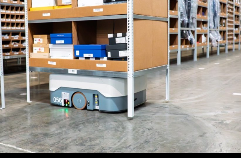 An autonomous mobile robot carrying shelving through a warehouse